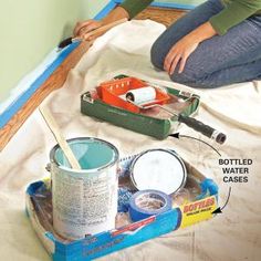 a woman sitting on top of a bed next to a paint can and some other items