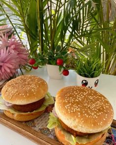 two hamburgers sitting on top of a wooden tray next to flowers and potted plants