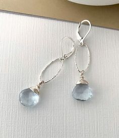 These beautiful faceted aquamarine quartz drop dangle earrings are available in vermeil gold or sterling silver.  They aquamarine heart briolettes are simply wire wrapped and dangle from textured, laser cut medium oval hoops finished with gold filled or sterling silver lever backs. Dainty & elegant dressed up or down.  These earrings make a perfect gift for a March birthday girl, bridesmaid or a special girl on any occasion! The earrings measure just approx 2" from end to end.  The aquamarine quartz approx 12mm.  Please make your preferred metal selection from the drop down menu at check out. If you should need multiple pairs please do not hesitate to contact me.  You may also like to check out more of my aquamarine jewelry here:  http://etsy.me/2FQujDr You may like to check out more of my Wire Wrapped Briolette Earrings, Blue Stone Earrings, Emma Style, Gemstone Hoop Earrings, March Birthday, Bling Earrings, Aquamarine Jewelry, Special Girl, Drop Dangle Earrings