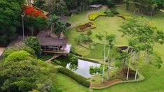 an aerial view of a house surrounded by lush green trees and shrubs, with a pond in the middle