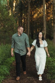 a man and woman walking through the woods holding hands