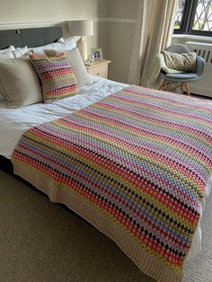 a bed with a colorful blanket on top of it next to a chair and window