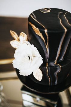 a black and gold cake with white flowers on top