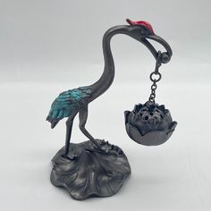 a metal bird figurine with a red hat on it's head holding a bowl