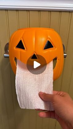 a person holding a roll of toilet paper in front of a halloween pumpkin shaped holder