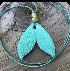 a blue necklace with a large wooden leaf on it's end and a beaded cord