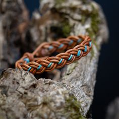 a brown and blue braided bracelet sitting on top of a rock next to some rocks