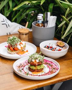 two white plates with food on them sitting on a table next to plants and bottles