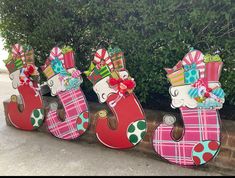 three wooden letters decorated with bows and presents are lined up against a brick wall in front of a bush