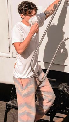 a man in white shirt and pink sweatpants standing next to a truck with his hand on the door handle