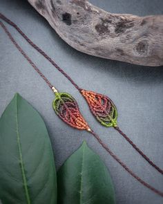 two beaded earrings sitting on top of a green leaf next to a wooden branch