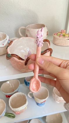 a person holding a spoon in their hand near bowls and cups on a shelf with other items