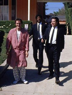 three men in suits are walking down the sidewalk