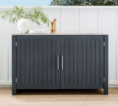 a black cabinet sitting on top of a hard wood floor next to a white fence