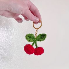 a crocheted cherry keychain being held by a person's hand