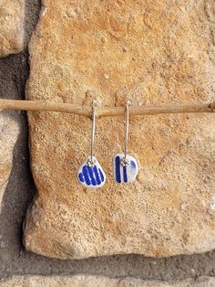 two small blue and white hearts hanging from silver earwires on a stone background