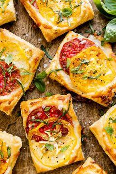 small square pizzas with tomatoes and herbs on a cutting board next to basil leaves