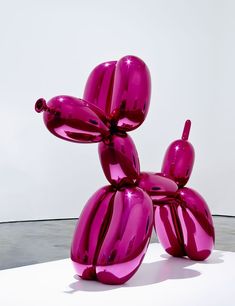 a pink balloon dog sculpture sitting on top of a white table next to a wall