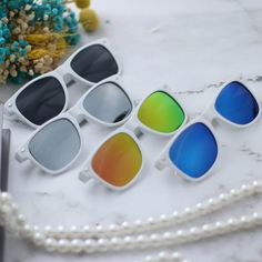 five pairs of sunglasses sitting on top of a white table next to a pearl necklace