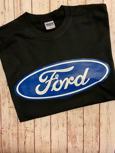 an old ford logo on a black t - shirt with blue and white lettering that says ford