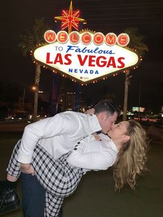 a man and woman kissing in front of the las vegas sign