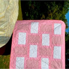 a pink and white quilt sitting on top of a grass covered field