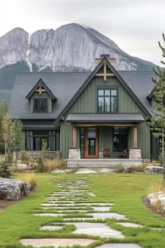 a green house with stone steps leading up to the front door and large mountains in the background