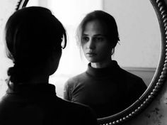 a woman standing in front of a mirror looking at her reflection on the wall,