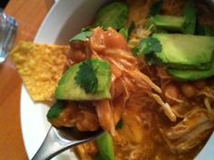 a white bowl filled with soup and topped with avocado, cilantro, and tortilla chips