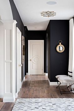 a hallway with black walls, white trim and wooden flooring has a bench in front of the door