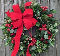 a christmas wreath with red berries and green leaves on a wooden fence next to a bush