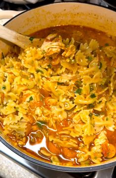 a pot filled with pasta and vegetables on top of a stove next to a wooden spoon