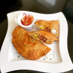 two pastries on a white plate with a small bowl of sauce