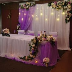 a table set up for a wedding with purple and white flowers on the table cloth