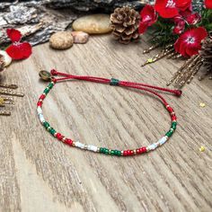 a red string bracelet sitting on top of a wooden table next to flowers and pine cones