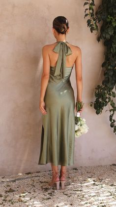 a woman standing in front of a wall wearing a green dress and holding a bouquet