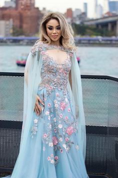 a woman wearing a blue gown with flowers on it and a cape over her head