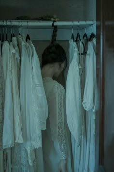 a woman is looking at wedding gowns hanging in a closet