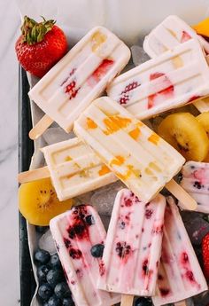 popsicles with fruit and ice cream sit on a tray next to bananas, strawberries, and blueberries