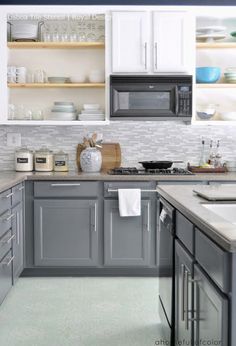 a kitchen with gray cabinets and white counter tops, along with dishes on the shelves