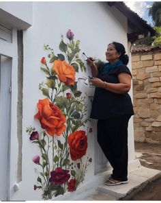 a woman painting flowers on the side of a building