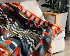 an orange, blue and green plaid blanket sitting on top of a couch next to a potted plant