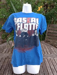 This is a Rascal Flats blue alstyle t shirt. Size small. It is used but strong graphics. it does have a small hole under armpit. Measurements are flat across shoulder 17", breast 19", hip 18 1/2" length lower shoulder down vertical 25". Casual Fitted Top For Fan Merchandise, Vintage Blue T-shirt With Front Print, Blue Band Merch T-shirt, Band Merch Blue T-shirt With Sublimation Print, Blue Pre-shrunk Shirt For Fan Merchandise, Blue Sublimation Print Tops For Fans, Blue Crew Neck Shirt With Front Print, Fitted Blue T-shirt With Text Print, Blue Fan Merchandise T-shirt For Summer