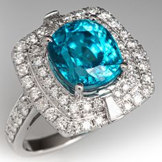 This gorgeous ring is centered with one (1) cushion mixed cut natural zircon set into a four-prong setting. The ring is also accented with fifty-six (56) bead set, round brilliant cut diamonds and channel set with two (2) tapered baguette cut diamonds. The ring measures 10.3mm at the top, rises 7.1mm above the finger, tapering to 4.3mm wide and 1.1mm thick at the base of the shank. It is currently a size 7. Luxury Cushion Cut Gemstones For Wedding, Luxury Cushion Cut Gemstones With Prong Setting, Cushion Cut Diamond Gemstones For Fine Jewelry, Cushion Cut Diamond Fine Jewelry, Luxury Diamond Topaz Ring With Cushion Cut, Luxury Cushion Cut Diamond Topaz Ring, Fine Jewelry Cushion Cut Gemstone With Center Stone, Elegant Cushion Cut Gemstone With Center Stone, Elegant Cushion Cut Gemstones