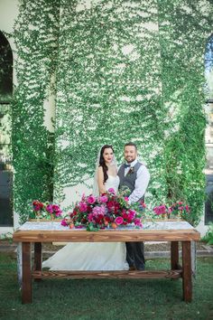 a bride and groom pose for a photo in front of an ivy covered wall