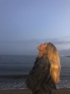 a woman standing on top of a beach next to the ocean looking up into the sky