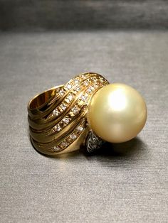 A large and impressive cocktail ring crafted in 18K yellow and white gold and centered by a 16.30mm golden south sea pearl surrounded by approximately .75cttw in G-I Vs2-Si1 clarity round diamonds. Dimensions/Weight: Ring measures .95" top to bottom and weighs 21.1g. Size 7 (sizable). Condition: All stones are secure and in perfectly wearable condition. R-GCVC Luxury Gold Pearl Ring With High Luster, Luxury High Luster Gold Pearl Ring, Pearl Cocktail Ring, Golden South Sea Pearls, Sea Pearl, Ring Crafts, South Sea Pearls, Sea Pearls, Diamond Gold