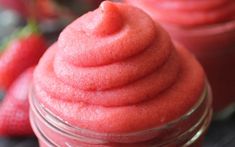 two jars filled with red colored food sitting on top of a table next to strawberries