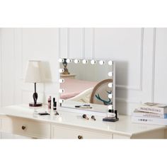 a white dresser with a mirror and lights on it's sides, next to a lamp