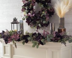 a wreath on top of a mantle with purple flowers and greenery